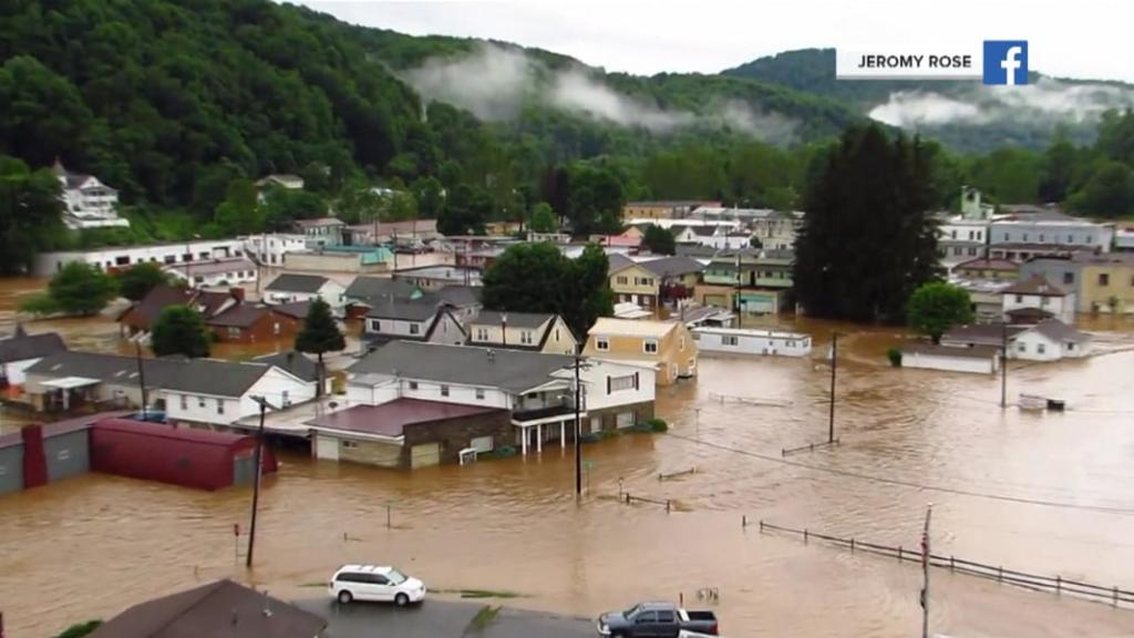 A photo showing a small town submerged in muddy water with a wooded mountain in the background