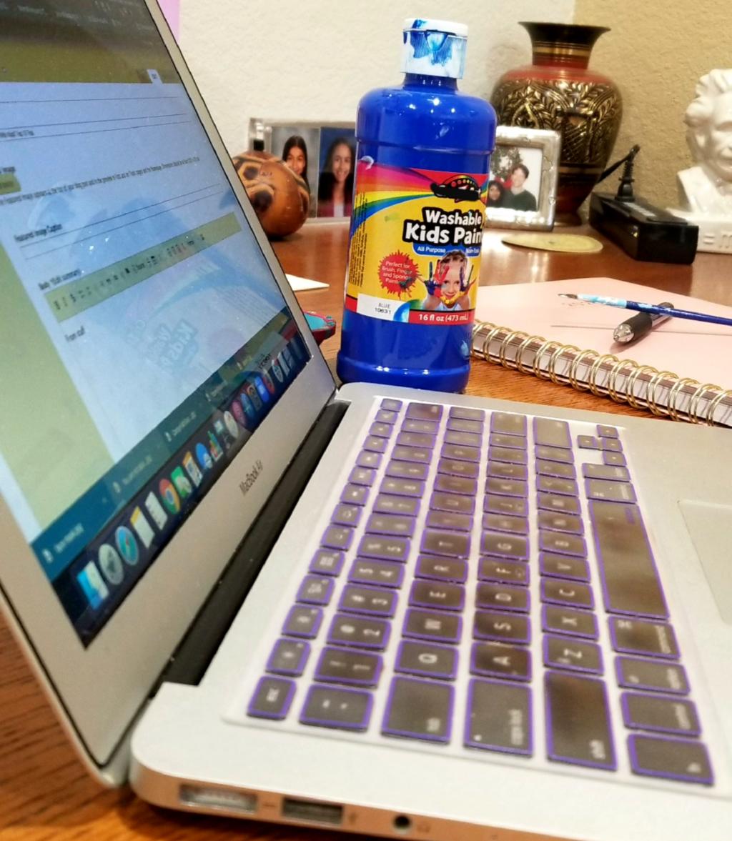[IMAGE DESCRIPTION: A photo of a laptop with a bottle of kids' paint, a paintbrush, a planner, and a pen in the background.]